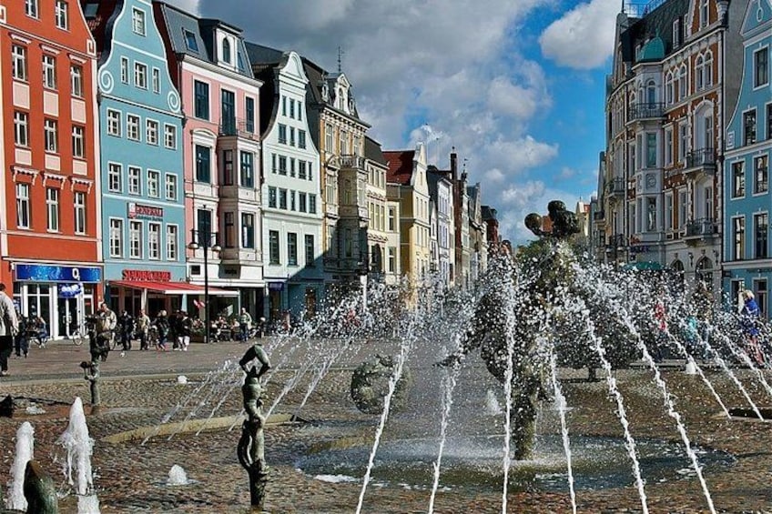 A public square with a fountain, colorful buildings, and pedestrians. 2
