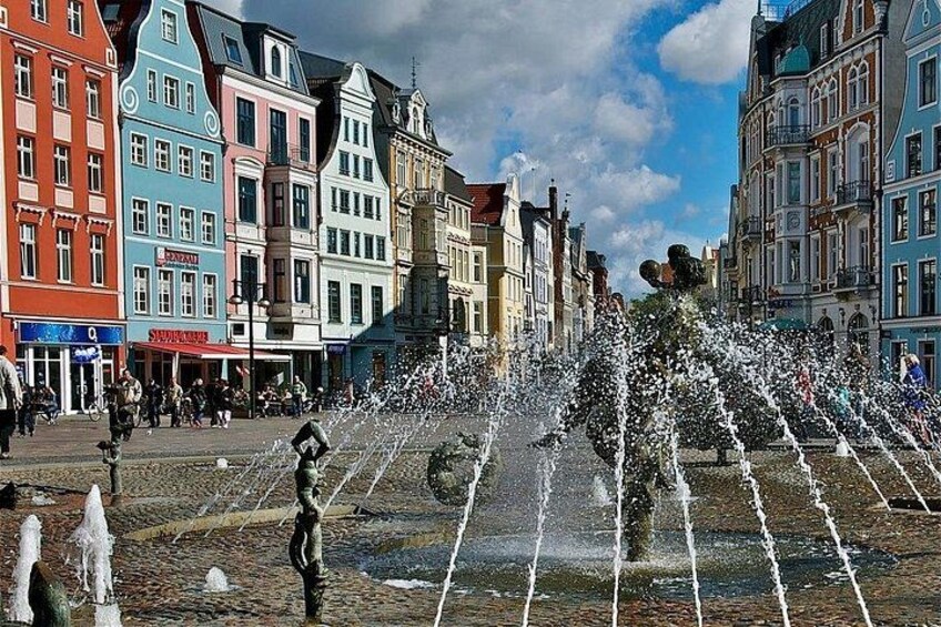 Ein öffentlicher Platz mit einem Brunnen, bunten Gebäuden und Fußgängern. 2