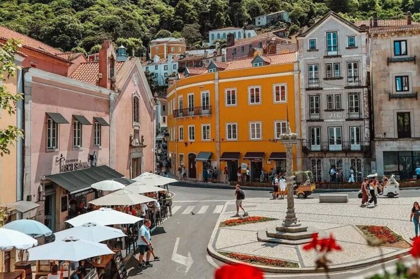 A street with colorful buildings, a roundabout, and outdoor seating areas. 5