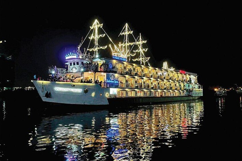 Een groot, verlicht schip met meerdere dekken en een opvallende mast, afgemeerd in de nacht. 1