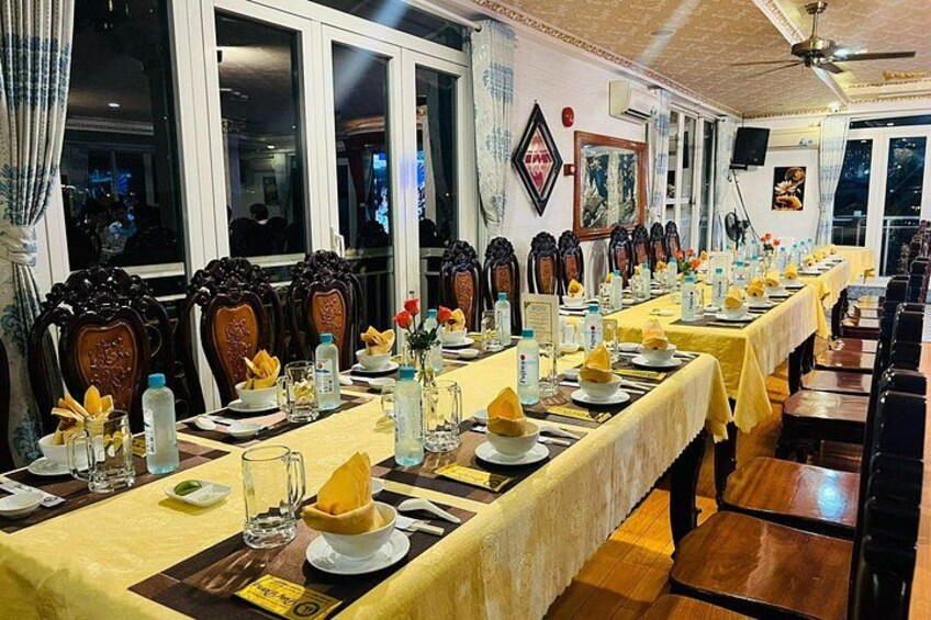 Een restaurant met lange tafels klaar voor diners, stoelen en een plafondventilator. 2