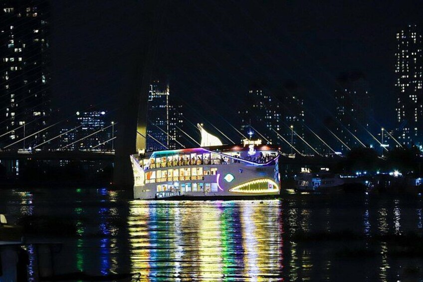 Een fel verlichte boot met een kleurrijk ontwerp, afgemeerd nabij een brug met verlichte gebouwen op de achtergrond. 4