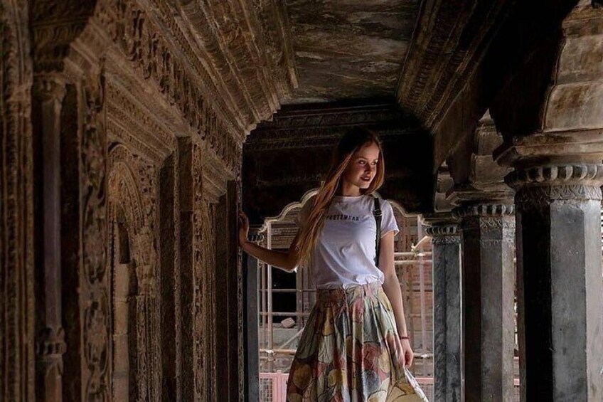 A person standing in an ornate architectural corridor with detailed carvings on the columns and walls. 5
