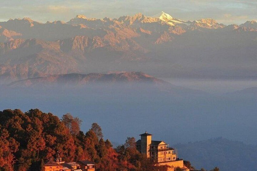 A mountainous landscape with a building on a hill and snow-capped peaks in the distance. 1