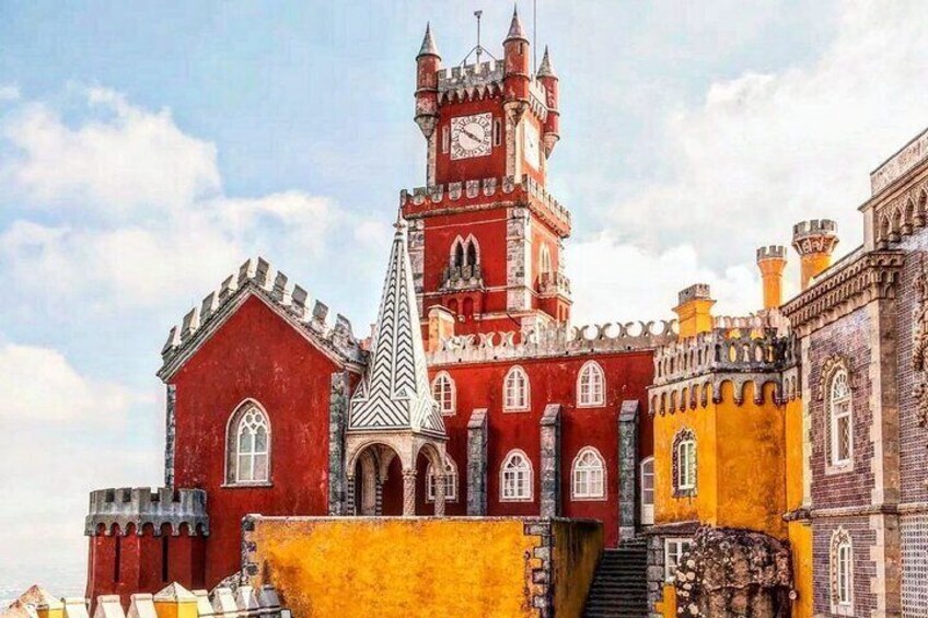 A castle-like building with red and yellow walls, a clock tower, and a pointed roof. 1