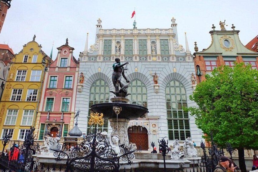 A historic building with ornate architecture, a statue on a fountain, and colorful surrounding buildings. 1