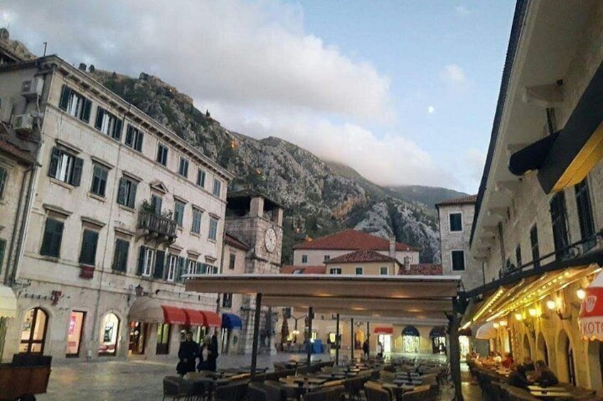 A historic square with buildings, a clock tower, and a mountainous backdrop. 3