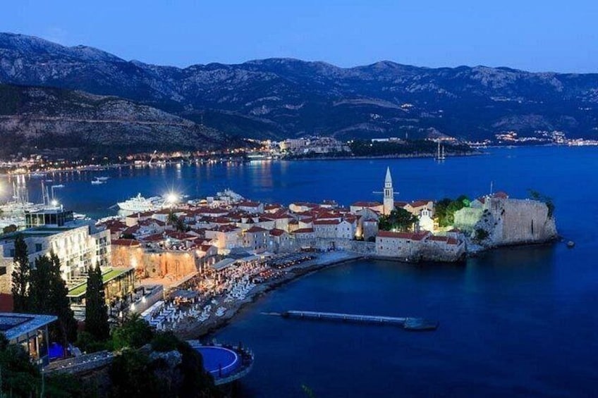 A coastal town with a fortified harbor, a prominent church tower, and a mountainous backdrop. 4