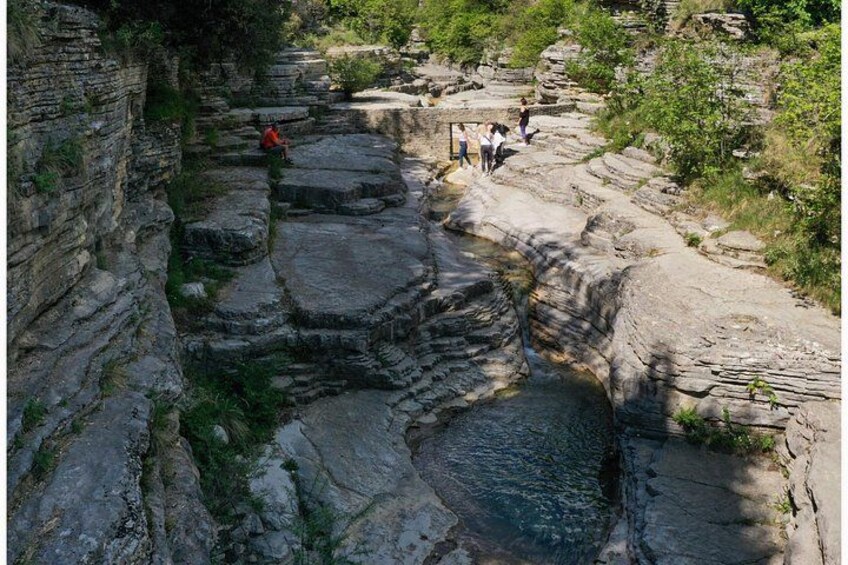 A rocky canyon with a narrow water channel, people walking along the path, and vegetation growing on the rocks. 4