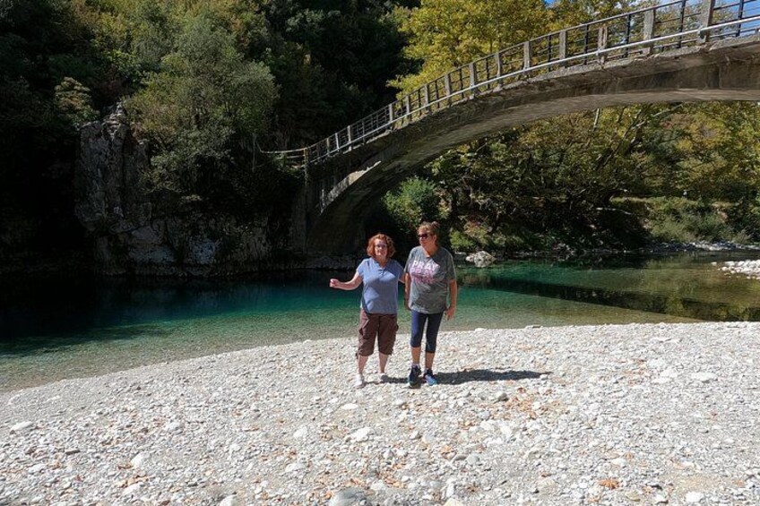 Two people standing on a rocky shore with a bridge in the background. 2