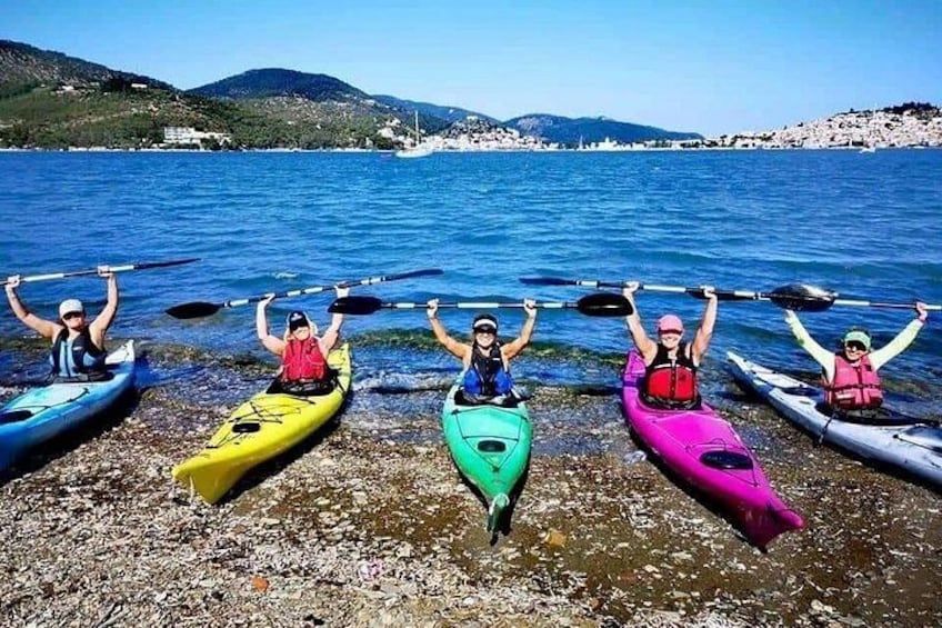 Five kayaks lined up on a rocky shore with a body of water and hills in the background. 2