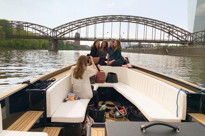 A boat with passengers on a river, a bridge in the background, and a cityscape. 2