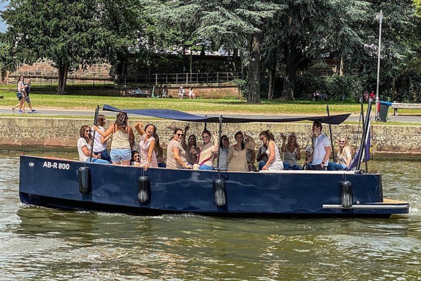 A boat with people on it, a body of water, and a park with trees and a fence in the background. 1