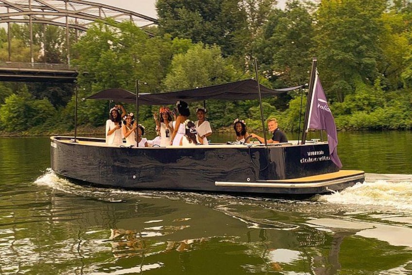A boat with people on it, moving on water, with greenery and a bridge in the background. 5