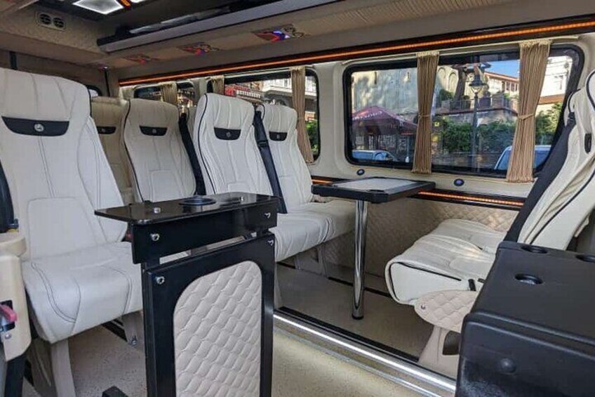 A train interior with white leather seats, a small table, and a window with curtains. 2