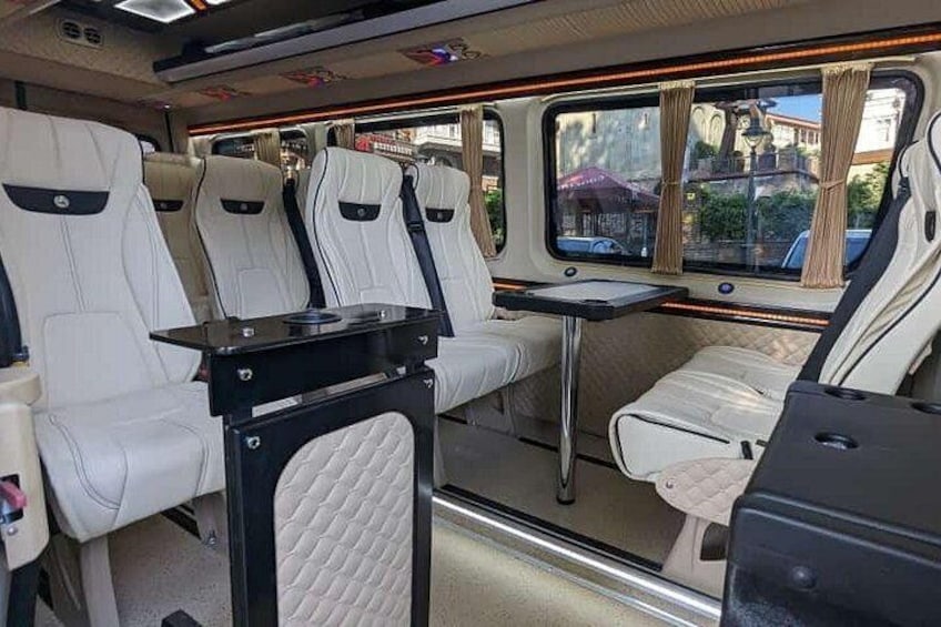A train interior with white leather seats, a small table, and windows with curtains. 4