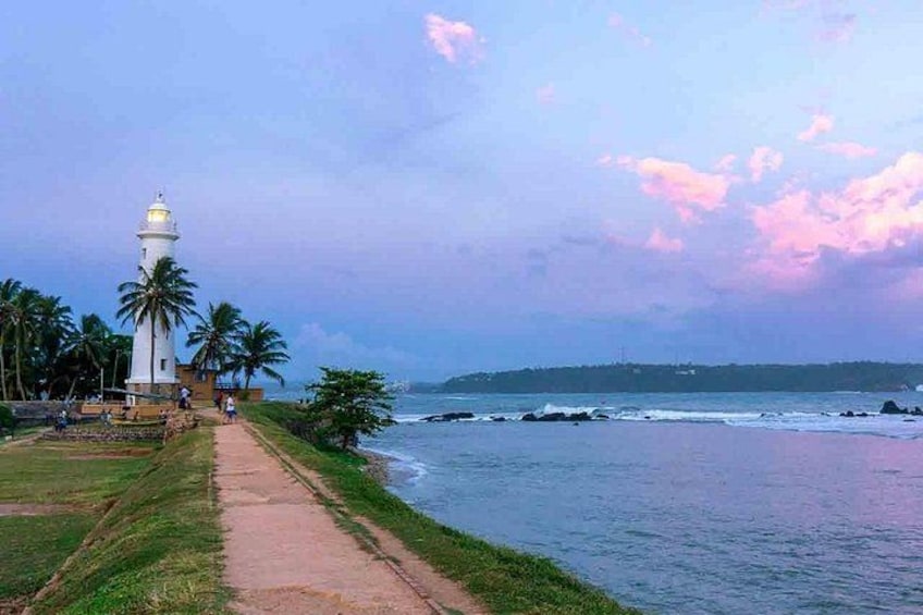 A coastal path with a lighthouse, palm trees, and a view of the sea. 3