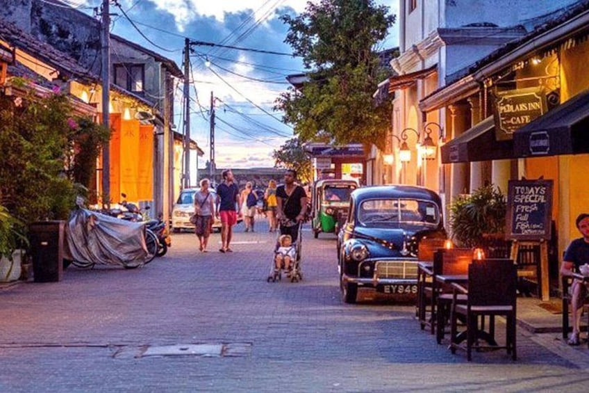 A street with shops, a vintage car, and people walking. 1