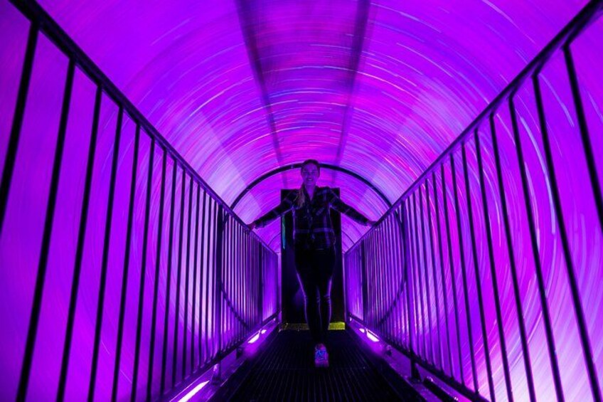 A person walking down a tunnel with purple lighting. 3
