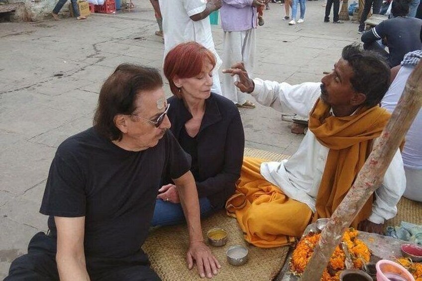 Three people sitting on the ground with a ceremonial setup including flowers and a metal bowl. 3