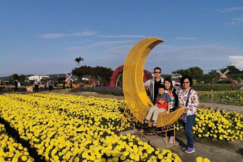 A family posing in front of a large crescent moon sculpture amidst a field of yellow flowers. 1