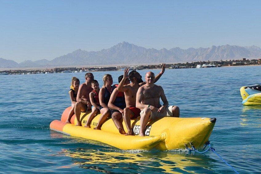 Un groupe de personnes se trouve sur un radeau gonflable jaune, sur une étendue d’eau, avec des montagnes en arrière-plan. 1