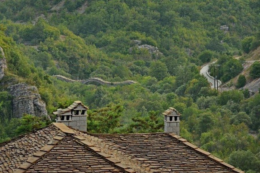A mountainous landscape with a winding road, stone chimneys, and a stone structure on a tiled roof. 2