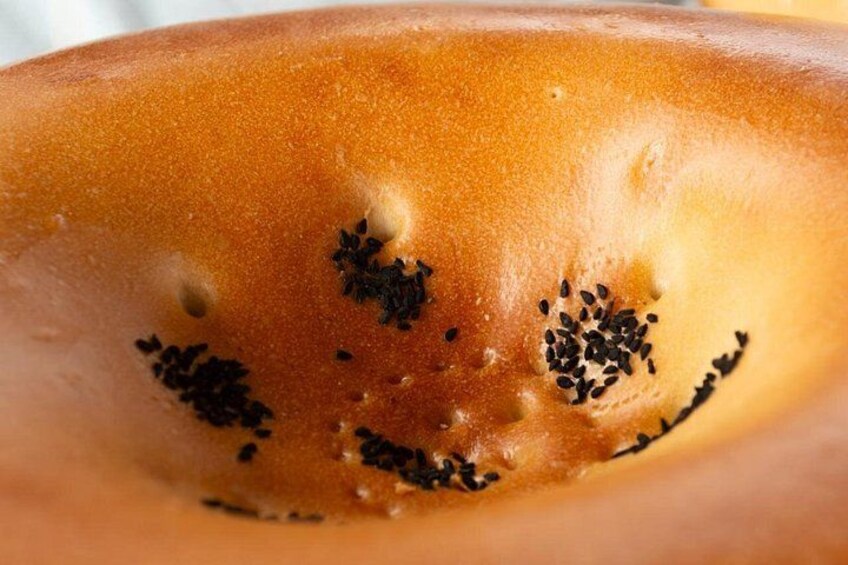 A close-up of a bread with sesame seeds and a smiley face drawn on it. 2