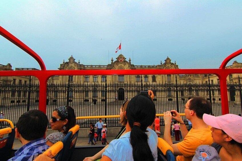 A group of people on a red bus, looking at a large, ornate building with a flag. 5