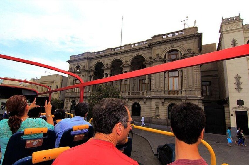 A group of people on a bus, a building with arches, and a red structure. 3