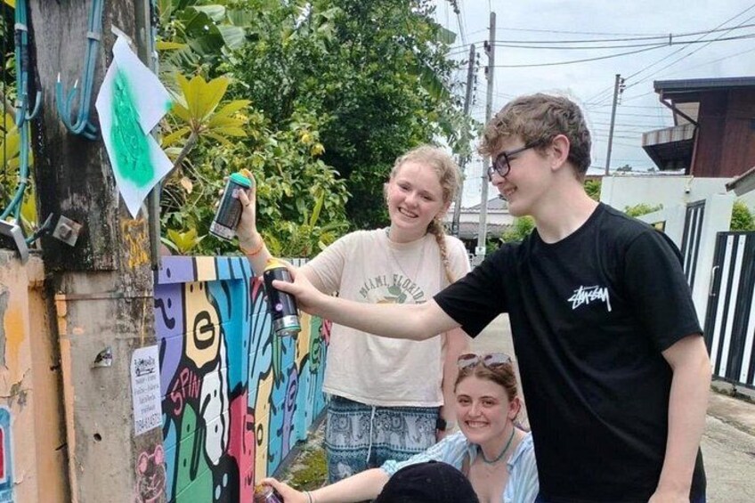 A person taking a photo with a smartphone, graffiti on a wall, and a tree in the background. 1