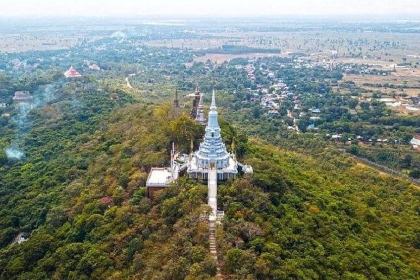 Et tempelkompleks med en central stupa omgivet af mindre bygninger, beliggende i et skovområde med udsigt til en by i det fjerne. 1