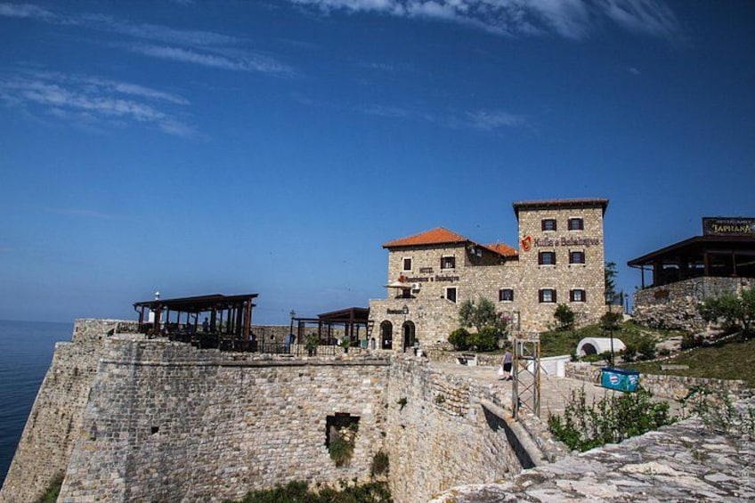 A stone fortification with a building on top, a clear sky, and the sea in the background. 3