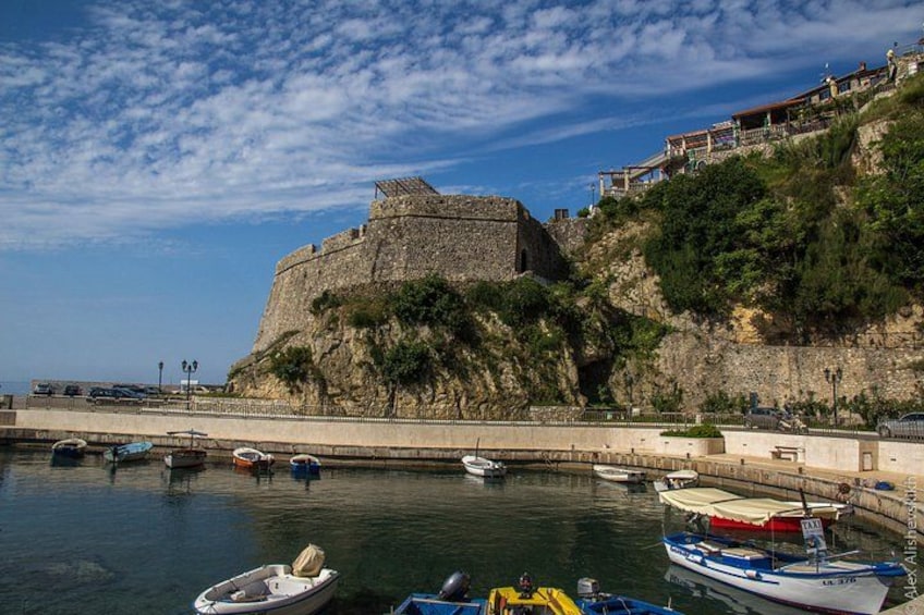 A coastal fortification, calm water with boats, and a clear sky. 2