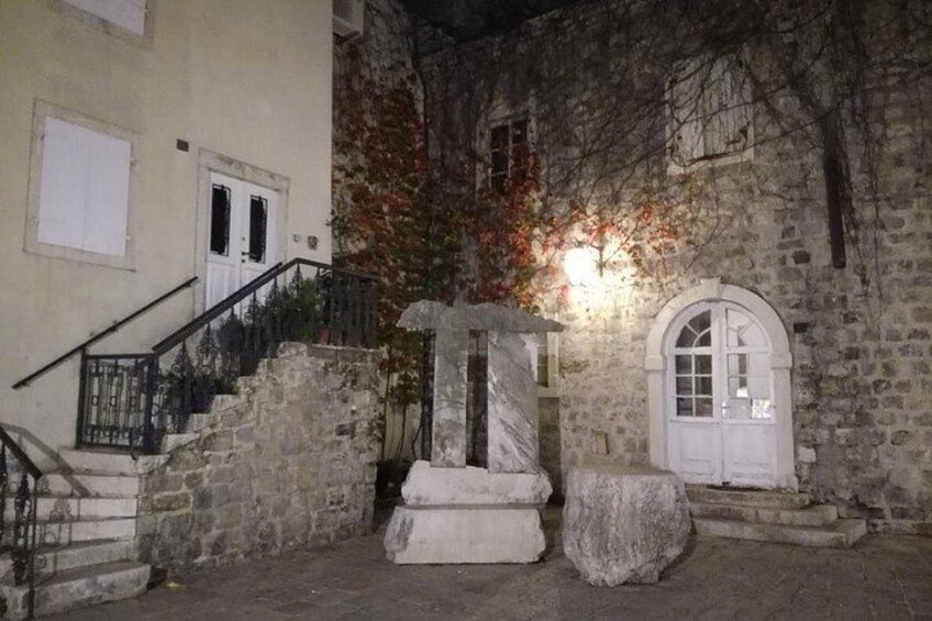 A stone building with a staircase, a white door, and a stone structure in front. 3