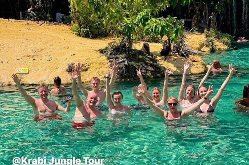 A group of people in a clear pool with a sandy beach and tropical vegetation in the background. 3
