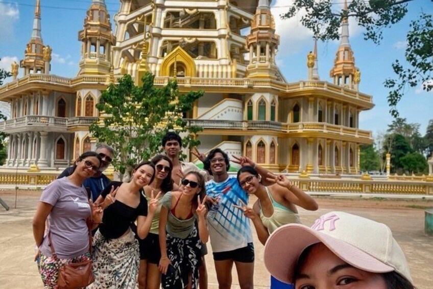 A group of people posing in front of a large, ornate building with multiple towers and golden accents. 2