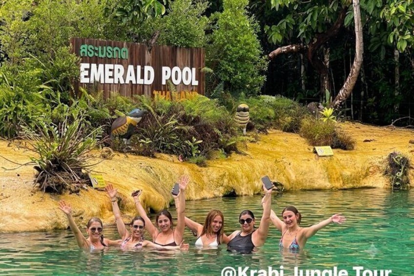 A group of people in a pool with a sign reading 'Emerald Pool' and a bird sculpture. 4