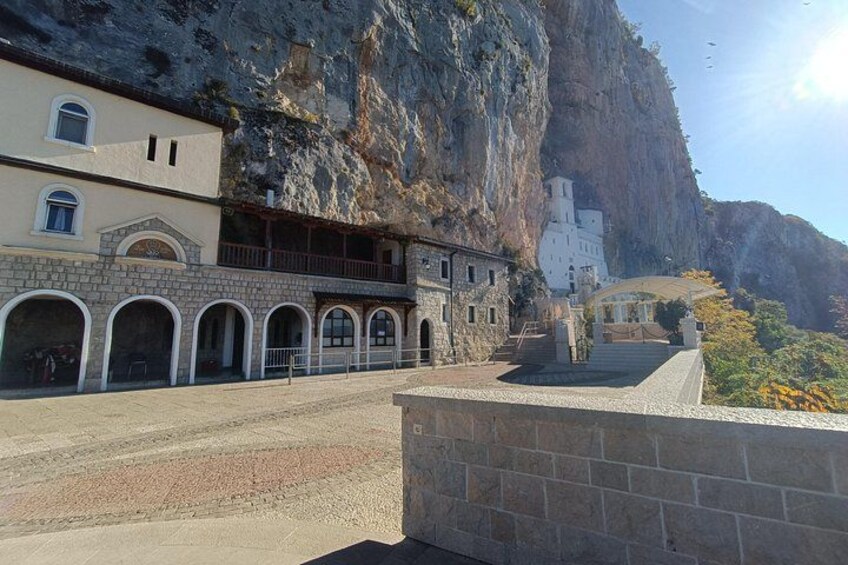 A coastal building with a stone facade, a white church with a bell tower, and a rocky cliff. 3