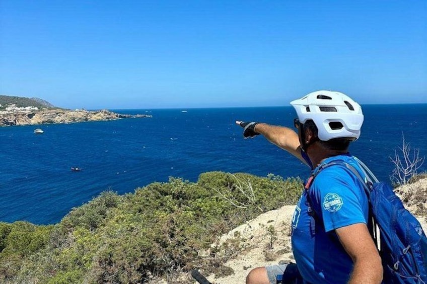 Eine Person mit Helm und blauem Hemd zeigt auf das Meer. 3