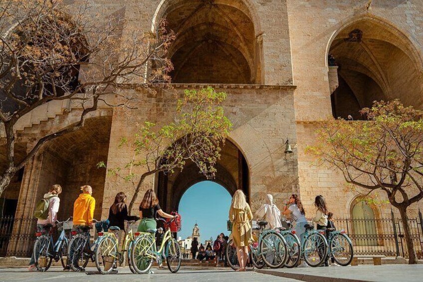 A group of people with bicycles in front of a historic stone archway. 1