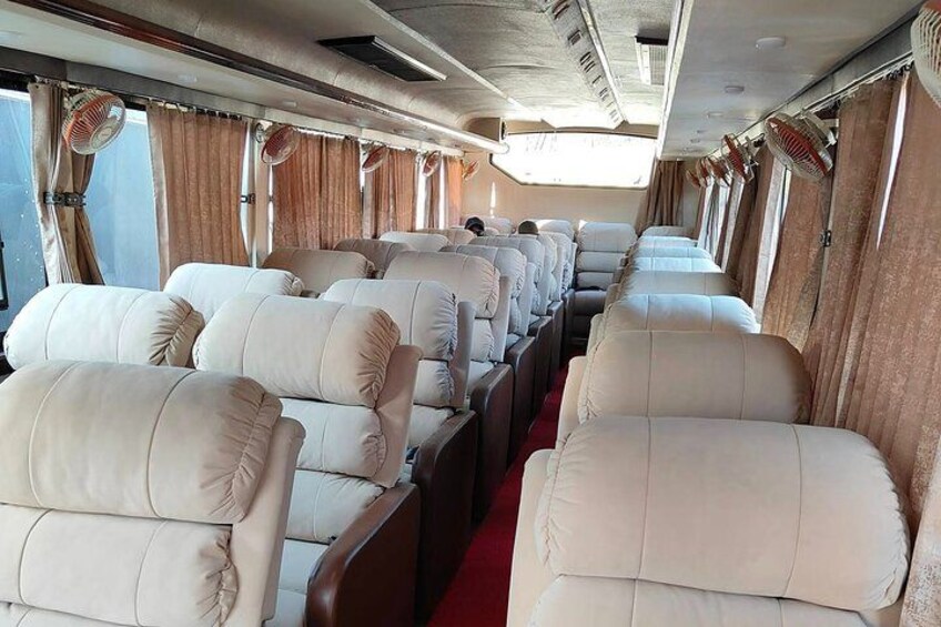 A train interior with rows of beige upholstered seats and overhead fans. 3