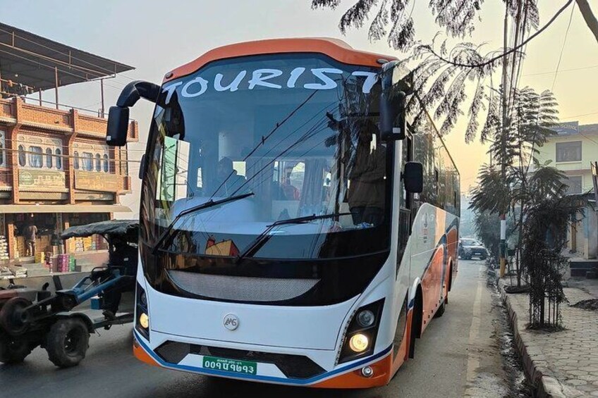 A white and orange bus with 'TOURIST' written on the front, parked on a street with buildings and trees in the background. 2