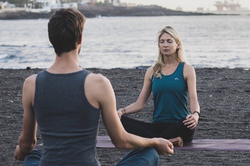 Two people sitting on a mat on a beach with the ocean in the background. 5