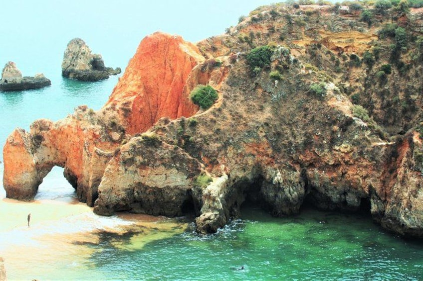 A coastal landscape with rocky cliffs, a clear blue sea, and a distinctive rock arch formation. 1