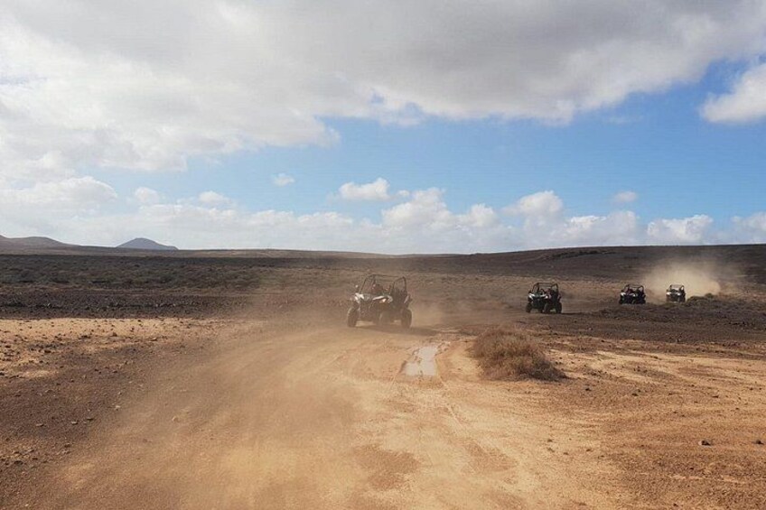 Off-road vehicles driving on a dusty road in a barren landscape with distant mountains. 4