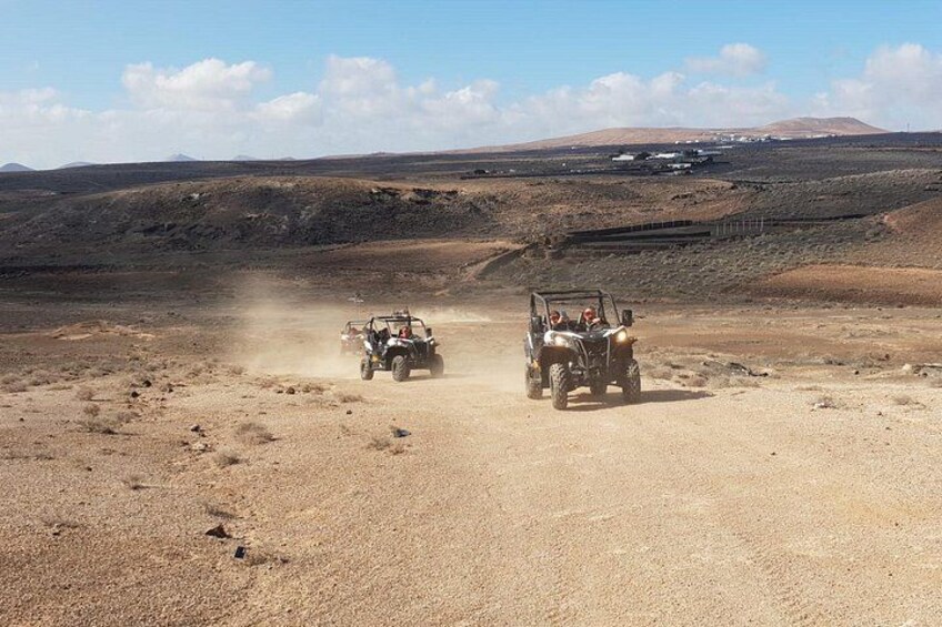 Two off-road vehicles driving on a dusty road in a barren landscape with distant hills. 2
