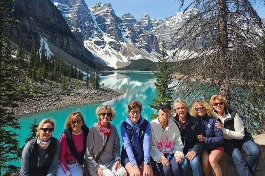 Un groupe de personnes est assis au bord d’un lac turquoise, avec des montagnes en arrière-plan. 1