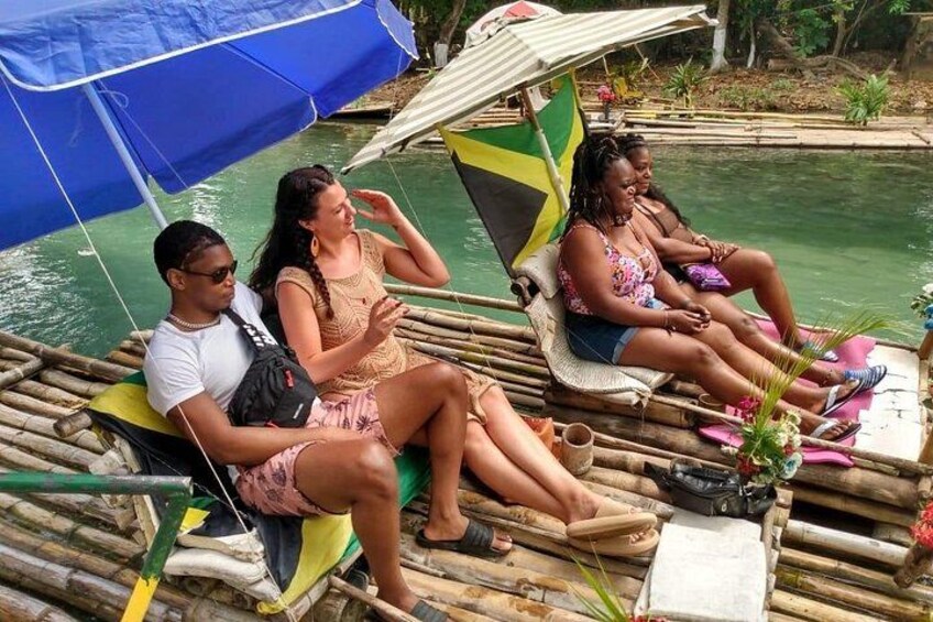 Personas sentadas en una plataforma flotante con una bandera, rodeadas de agua y vegetación. 1