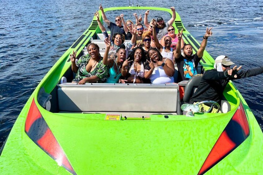 Un grupo de personas en un bote verde, con las manos levantadas, sobre una masa de agua. 1